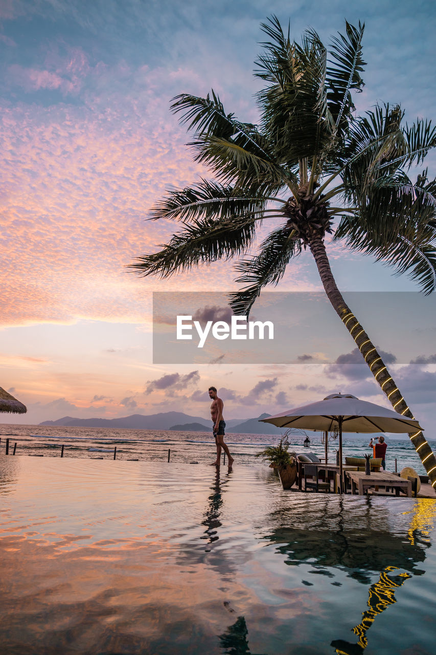 Man at infinity pool against sky at sunset