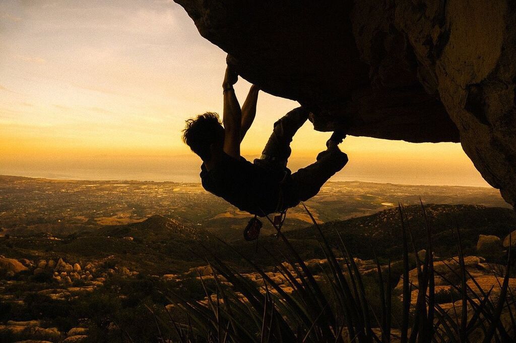 Man climbing on rock against sky during sunset