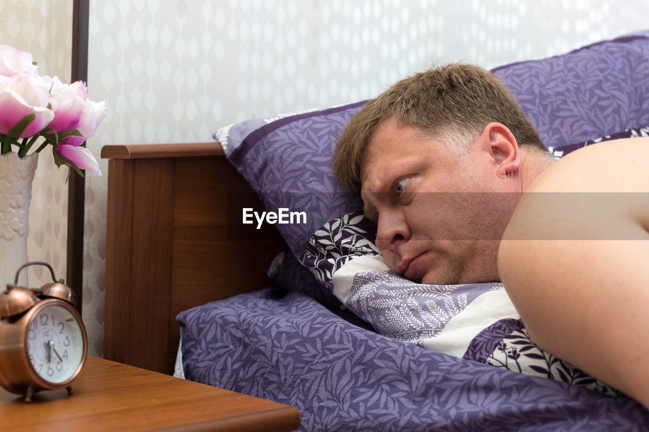 An agitated man looks at the alarm clock in horror, overslept for work.