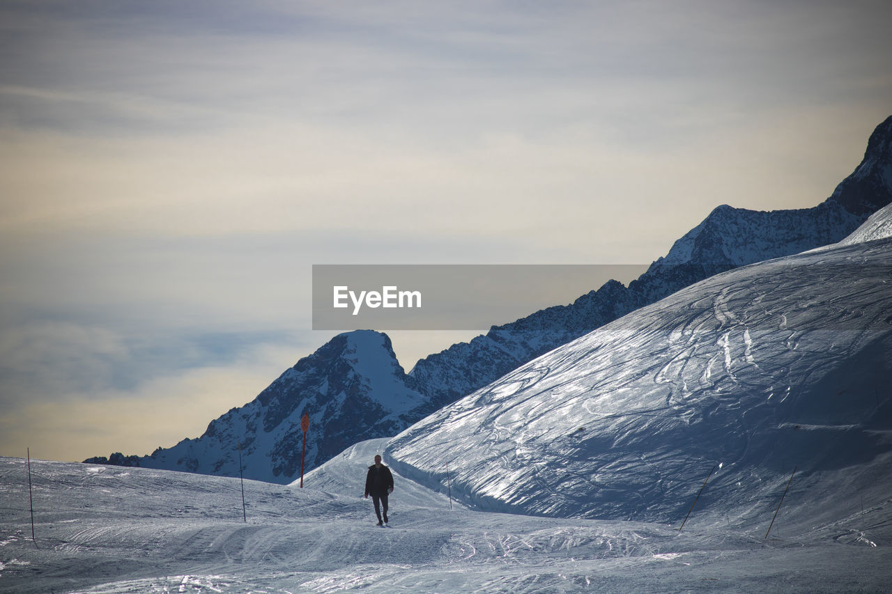 Man walking on snowcapped mountain against sky