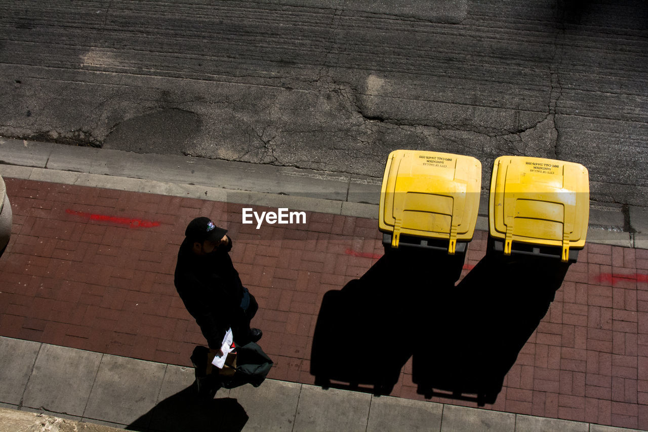 High angle view of man walking by yellow garbage cans on sidewalk