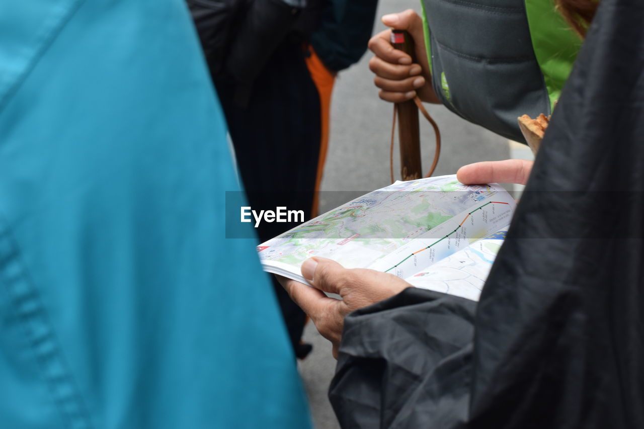 Midsection of people analyzing map while standing outdoors