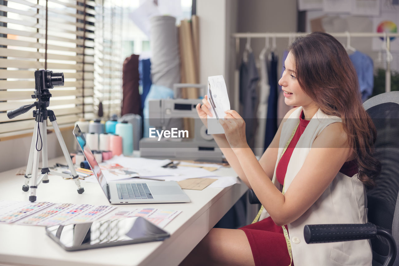 A lovely asian woman fashion designer sits at her workstation in her studio, stares video call.