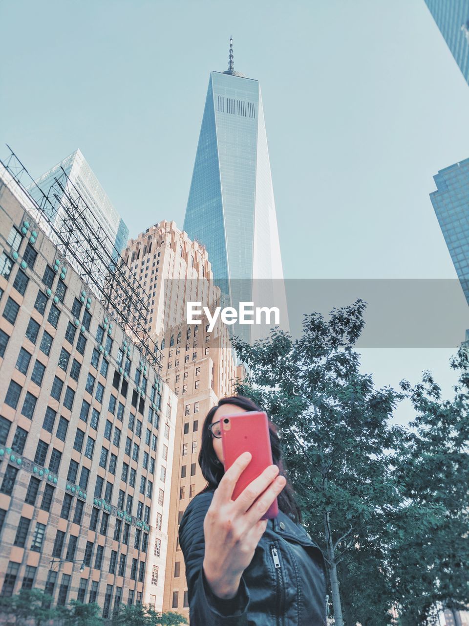 Low angle view of mid adult woman using mobile phone while standing against sky in city