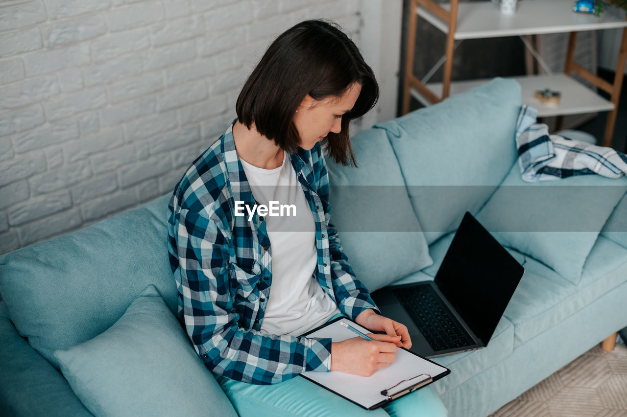 Young woman using laptop while sitting on sofa