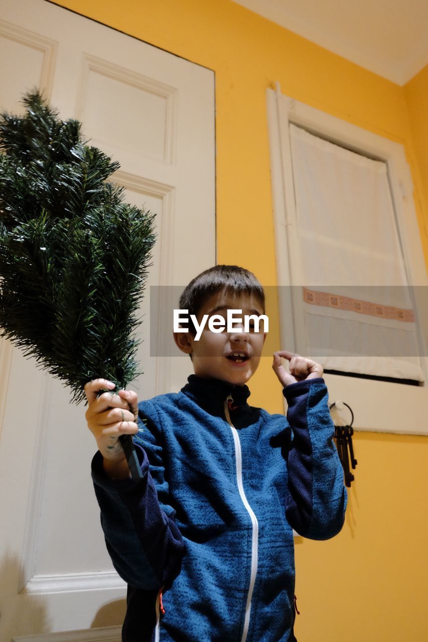 Boy holding christmas tree while standing at home