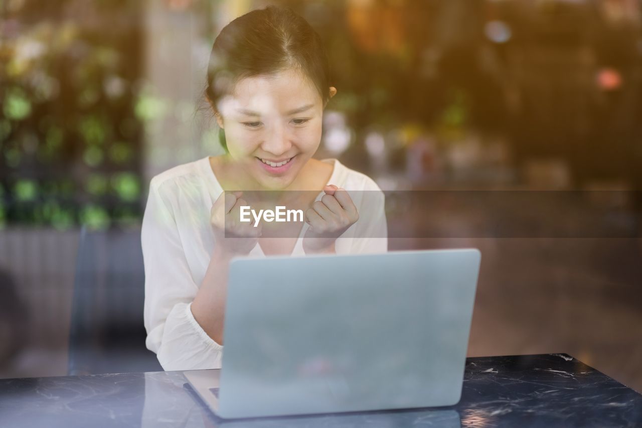 WOMAN LOOKING AT CAMERA WHILE SITTING ON MOBILE PHONE IN LAPTOP