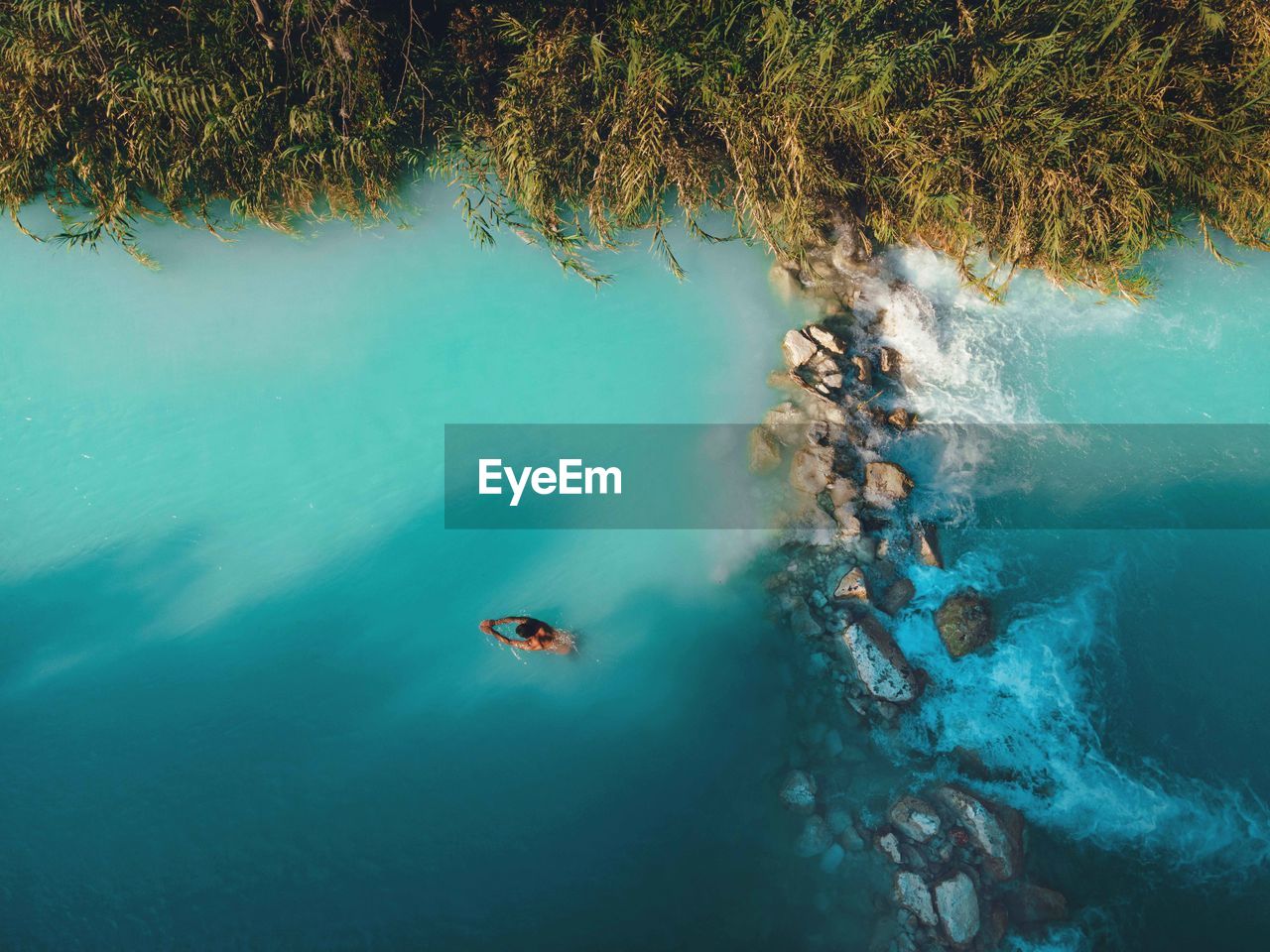 Aerial drone view of man swimming in tropical blue hot springs river