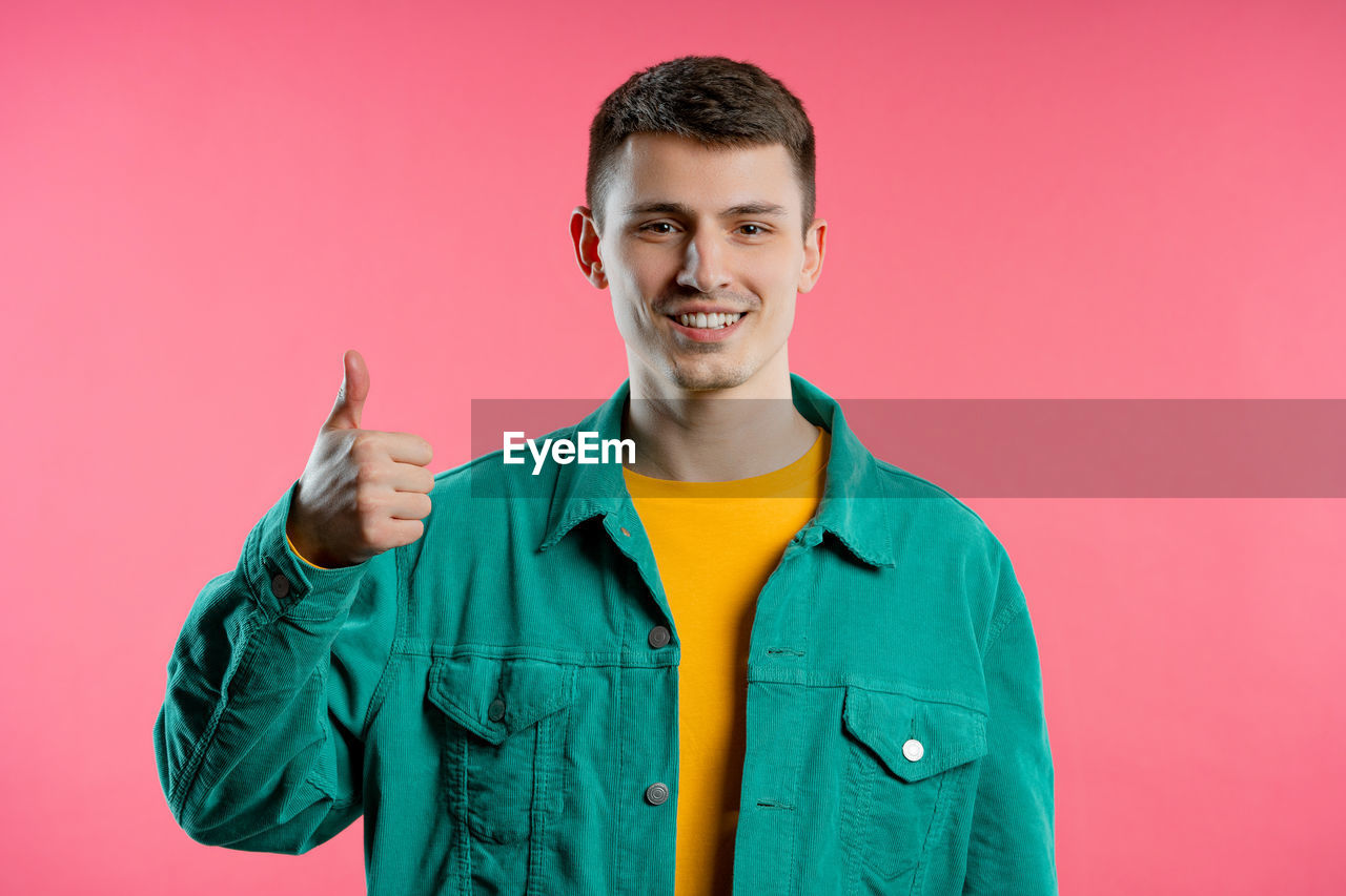 smiling, portrait, colored background, happiness, one person, studio shot, looking at camera, emotion, young adult, cheerful, adult, men, waist up, outerwear, indoors, front view, teeth, smile, positive emotion, standing, casual clothing, jacket, clothing, sleeve, person, pink background, fun, enjoyment, hood, copy space, lifestyles, green, individuality