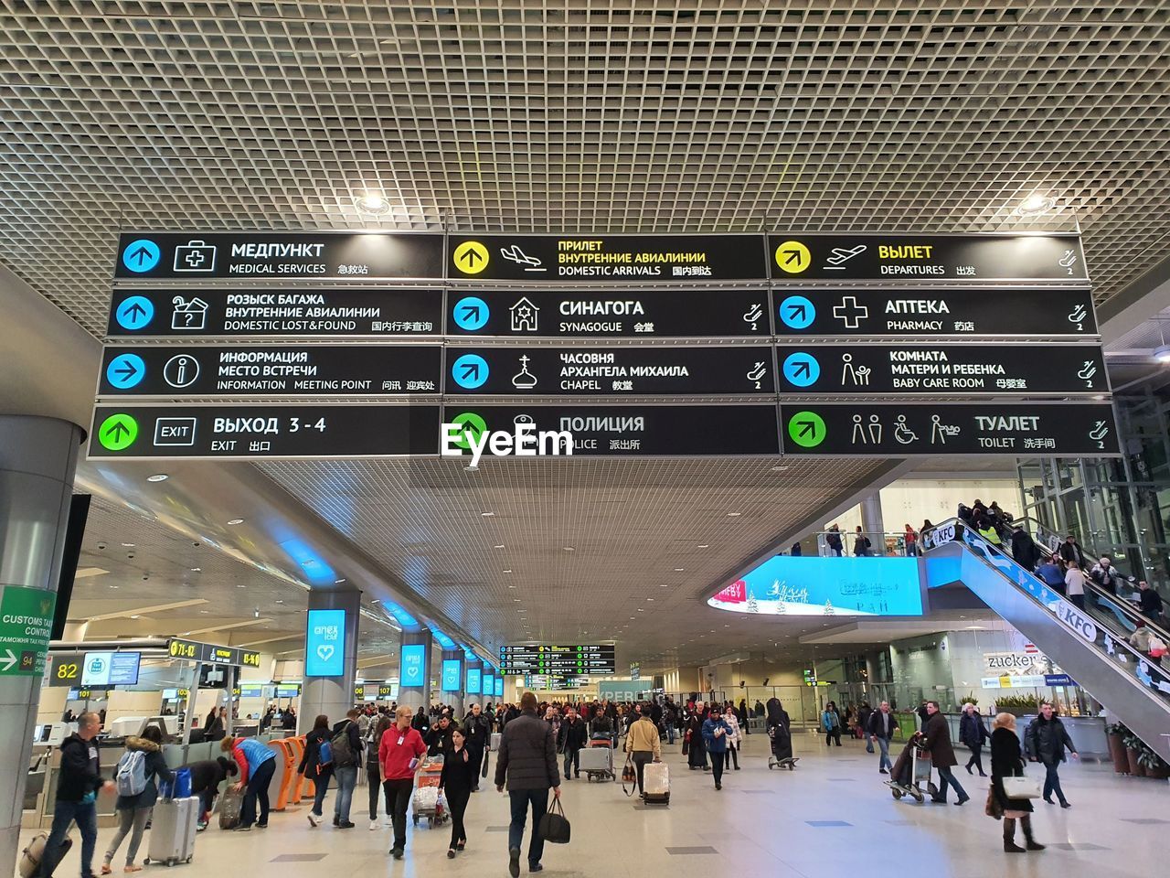 travel, crowd, large group of people, group of people, transportation, sign, airport, architecture, infrastructure, communication, journey, airport terminal, travel destinations, arrival departure board, guidance, information sign, directional sign, city, text, tourism, walking, built structure, indoors, arrow symbol, mode of transportation, airport departure area, city life, railroad station, holiday, airport check-in counter, passenger, public transport, men, illuminated, trip, vacation, motion