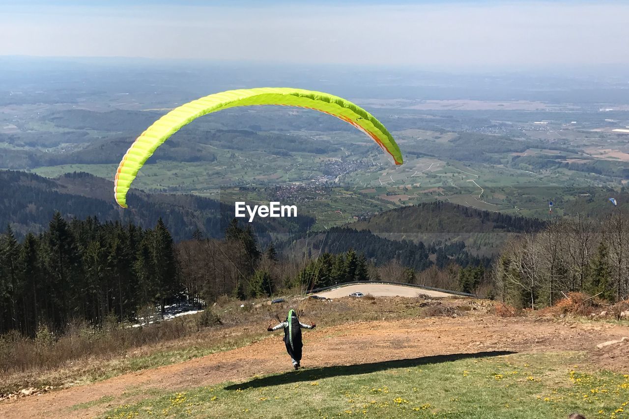 MAN FLYING OVER MOUNTAIN AGAINST SKY