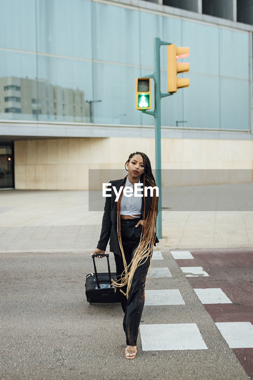 Young businesswoman with suitcase crossing street