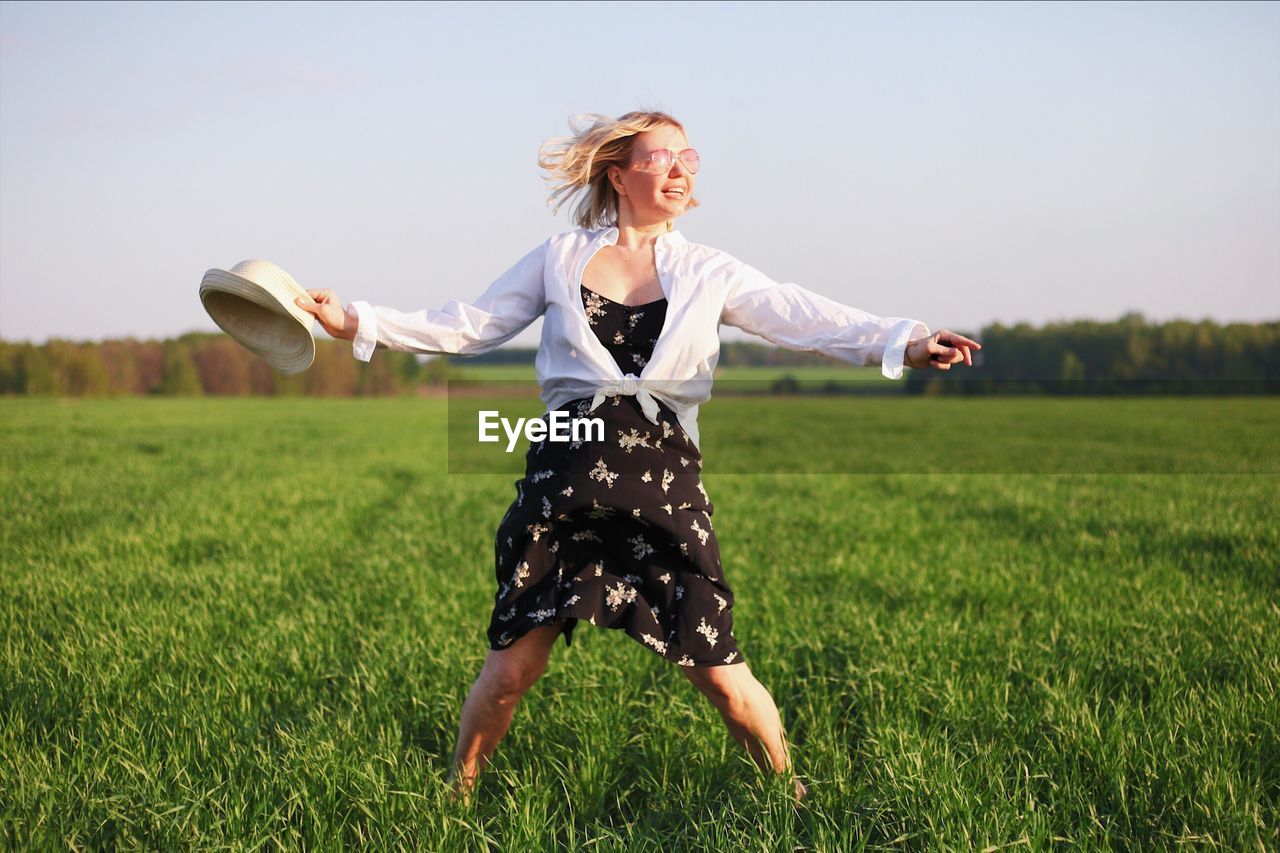 Woman with arms outstretched standing on land against sky