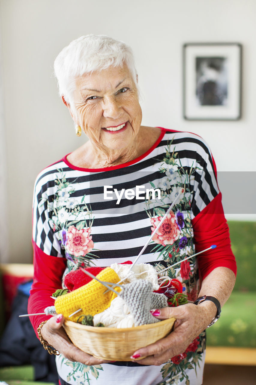 Portrait of happy senior woman holding knitting basket at nursing home