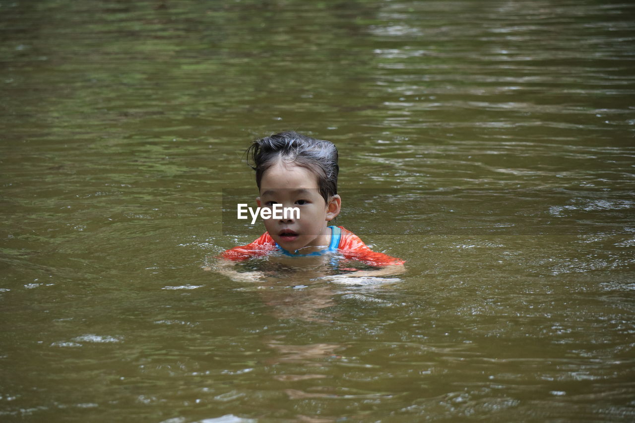 Boy looking away while swimming in lake
