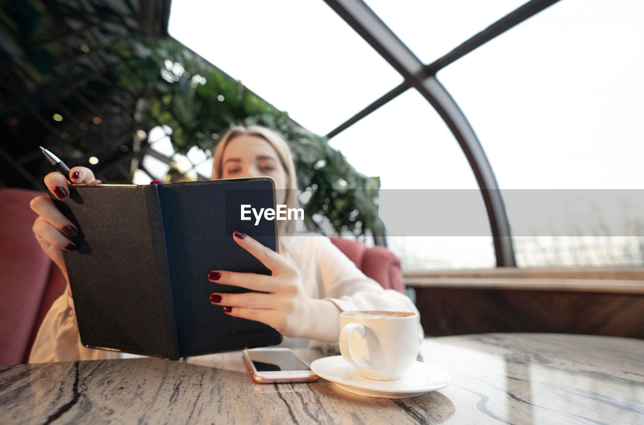 Woman holding coffee cup with mobile phone in cafe