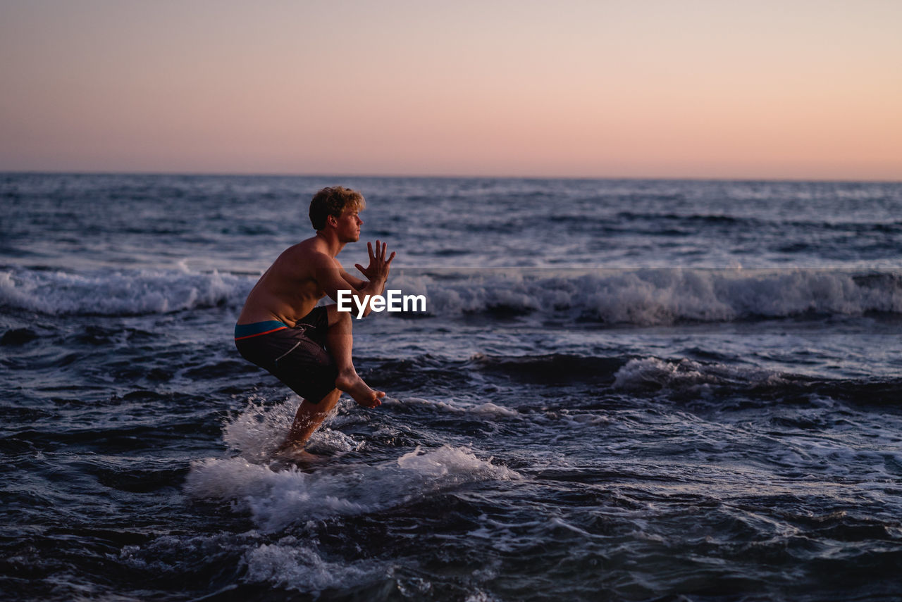 Full length of man exercising on shore at beach against clear sky