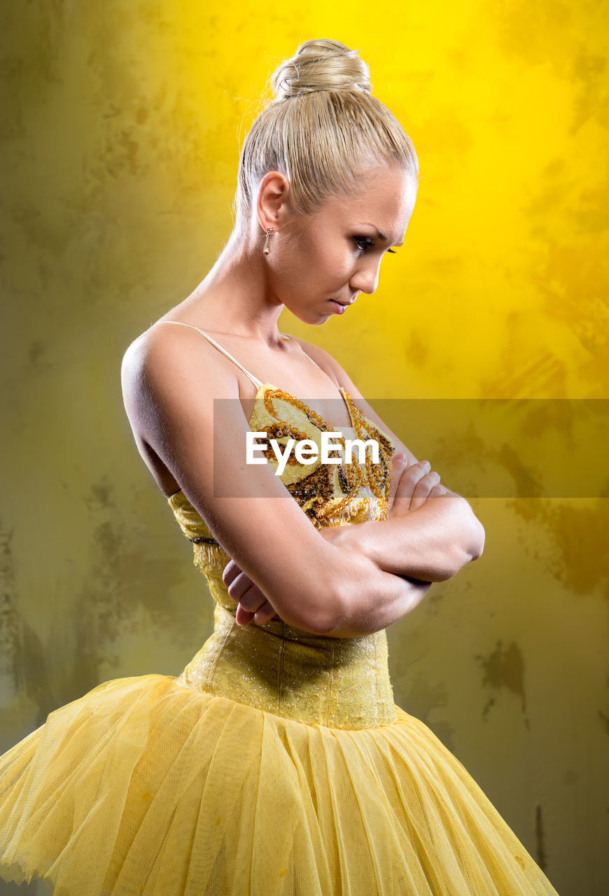 Ballerina wearing costume with arms crossed standing against yellow background