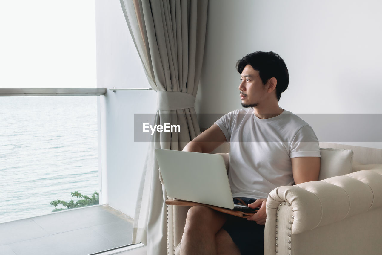 Man using laptop while looking away sitting at home