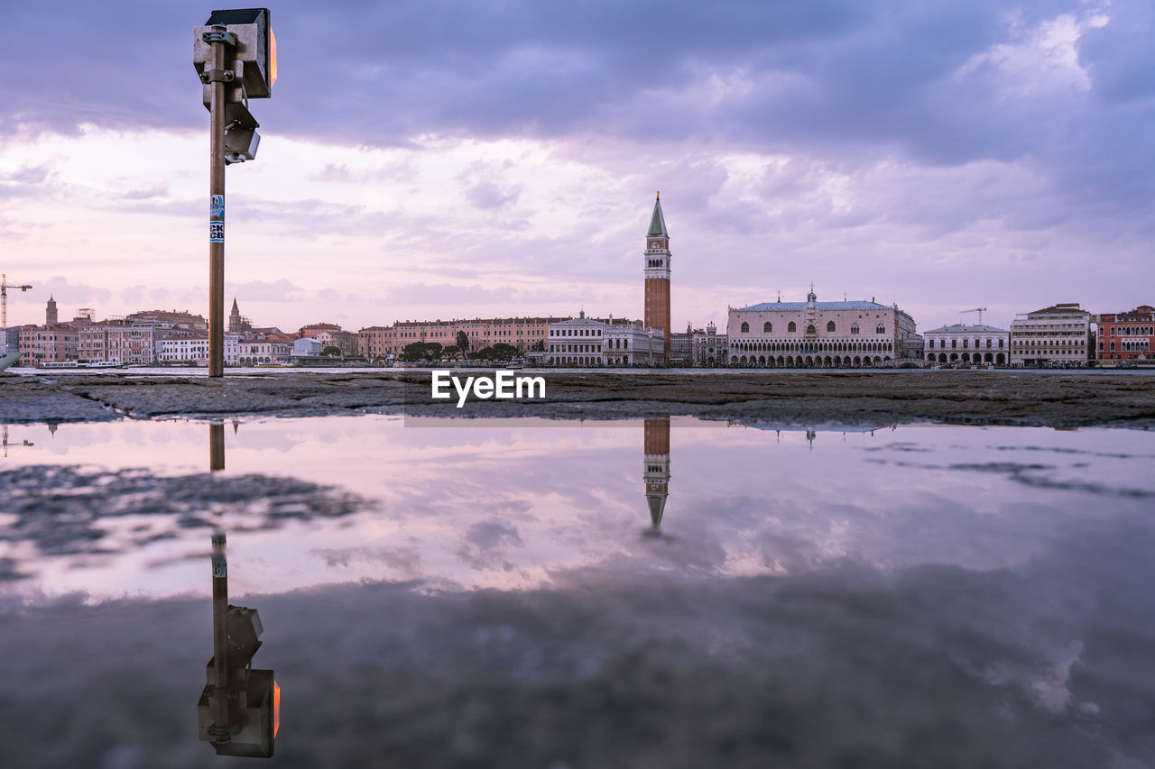 Lake by buildings in city against sky during sunset