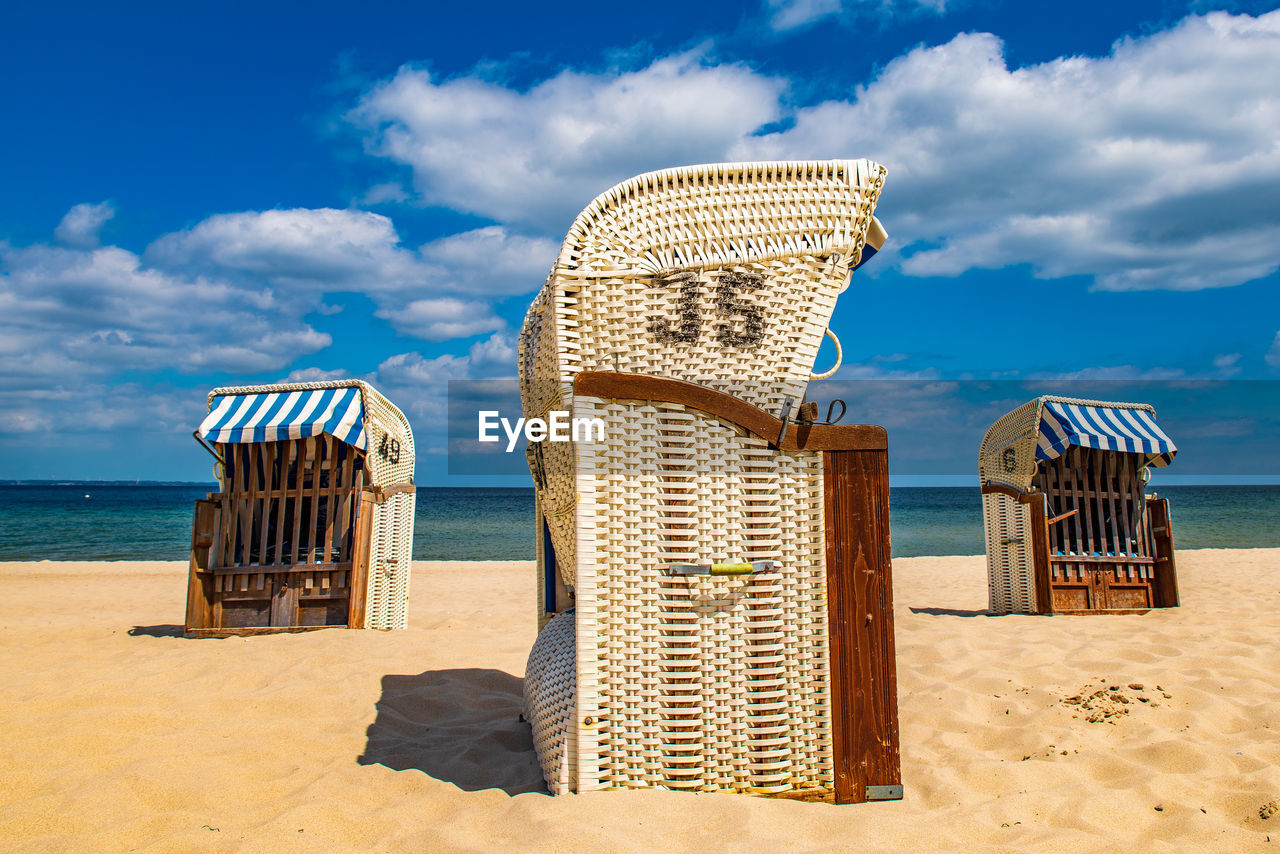 Hooded chairs on beach against sky