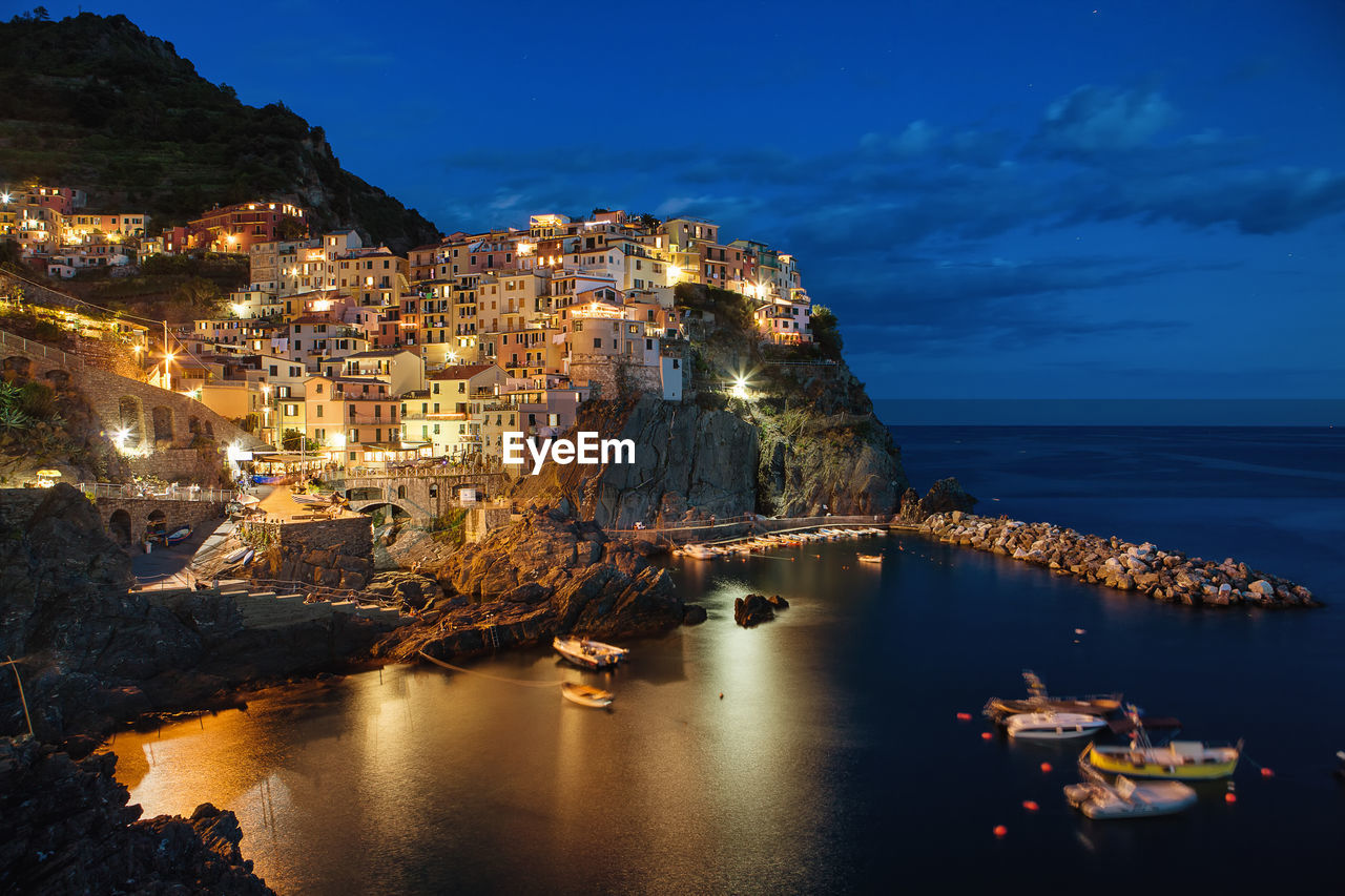 Aerial view of illuminated buildings by sea against sky