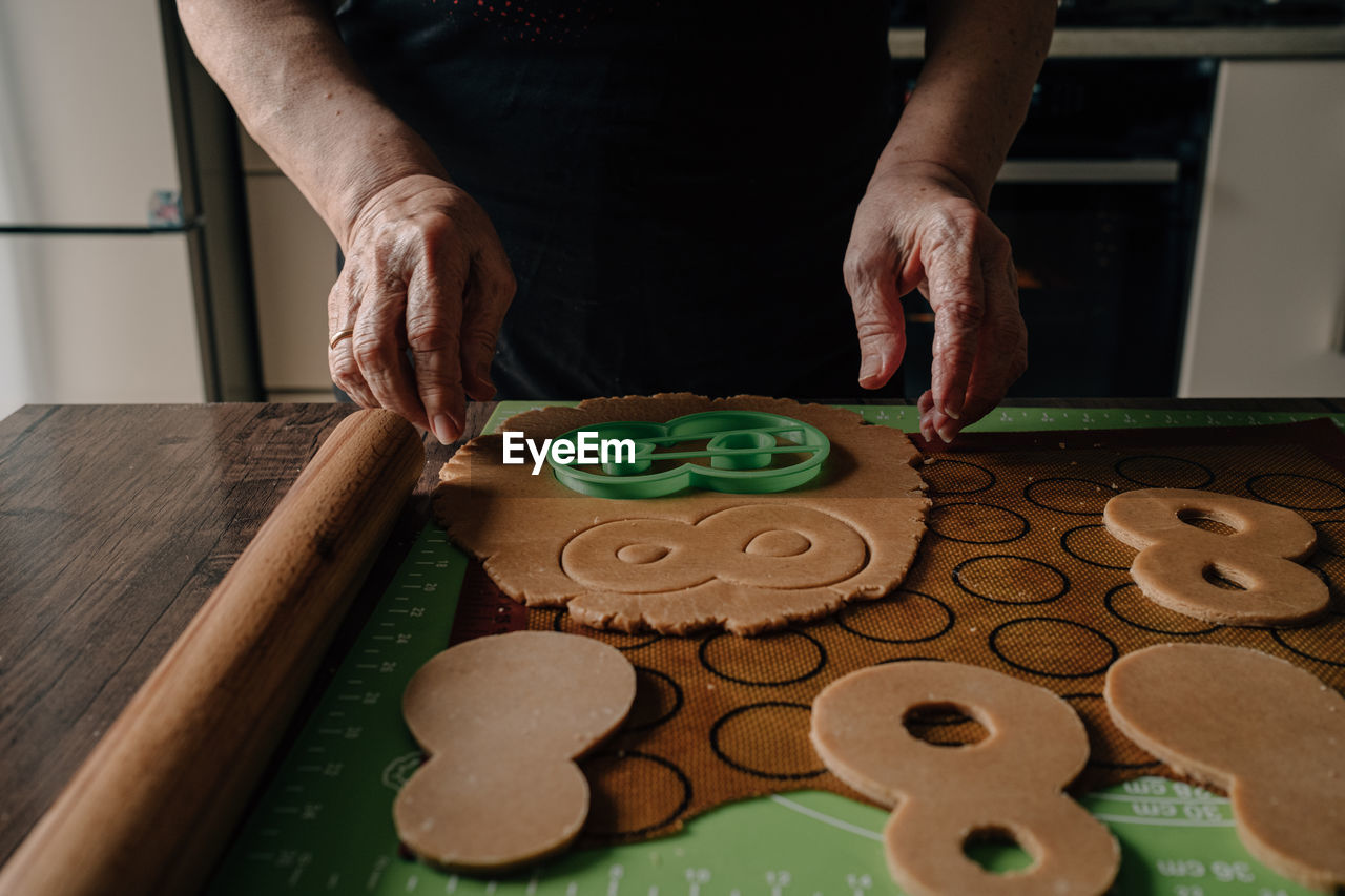 Grandmother makes gingerbread cookies with hands and cuts out figure eights for march 8