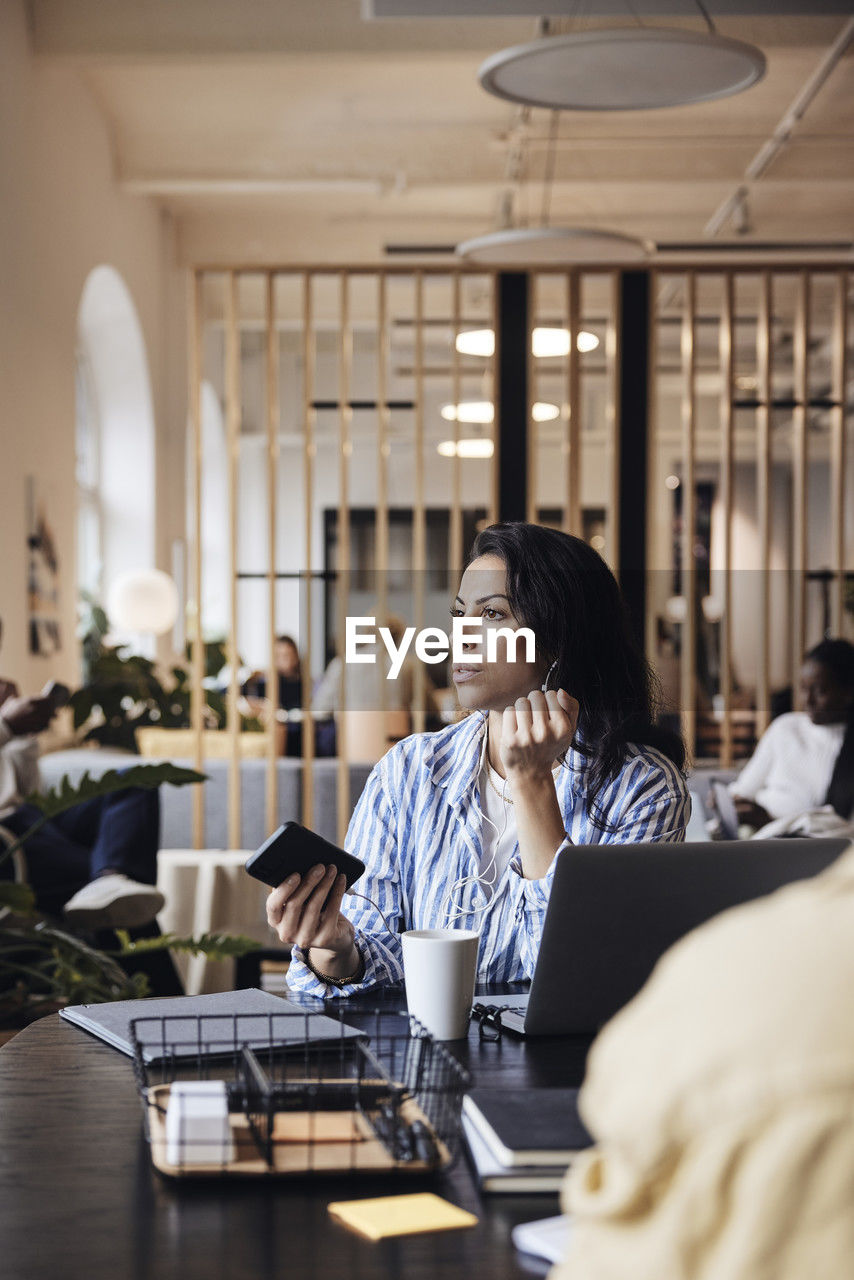 Female entrepreneur talking on smart phone while looking away at coworking office