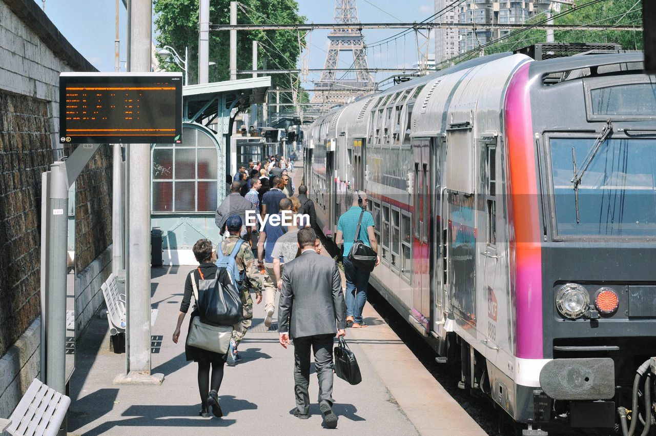 People at station with train against eiffel tower