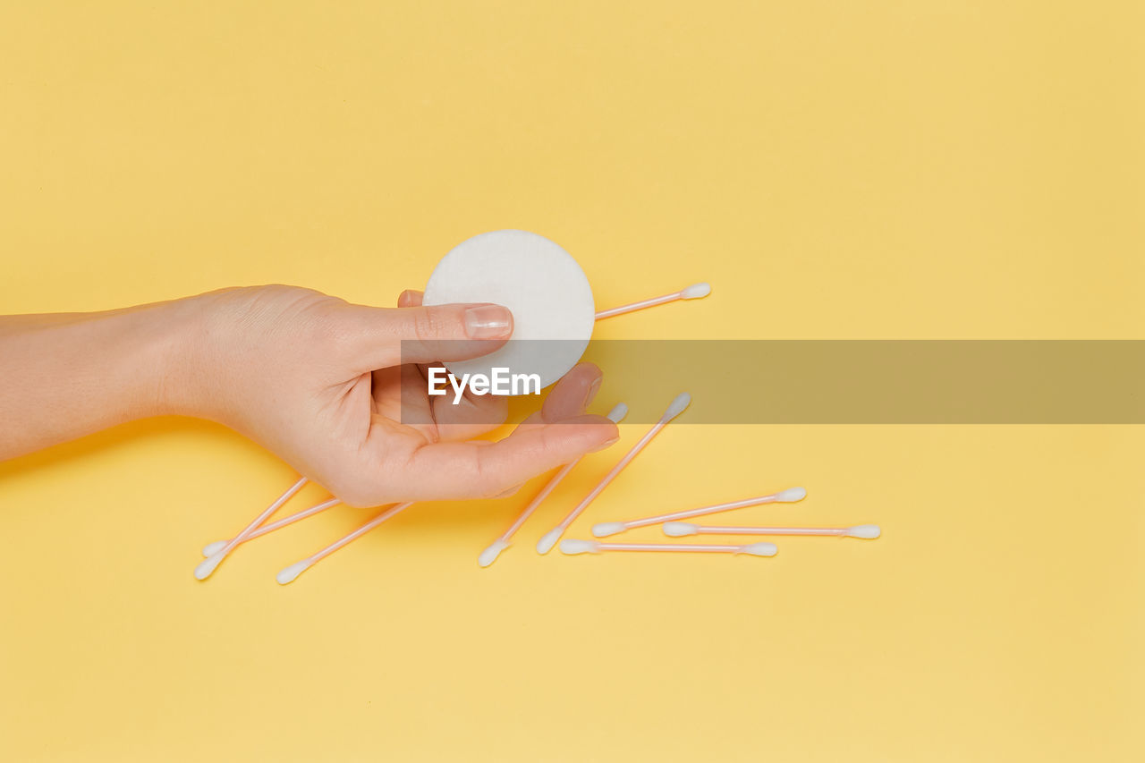 cropped hand of person holding thermometer against yellow background