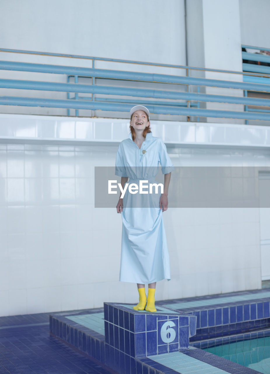 Smiling teenage girl looking away while standing at poolside against wall