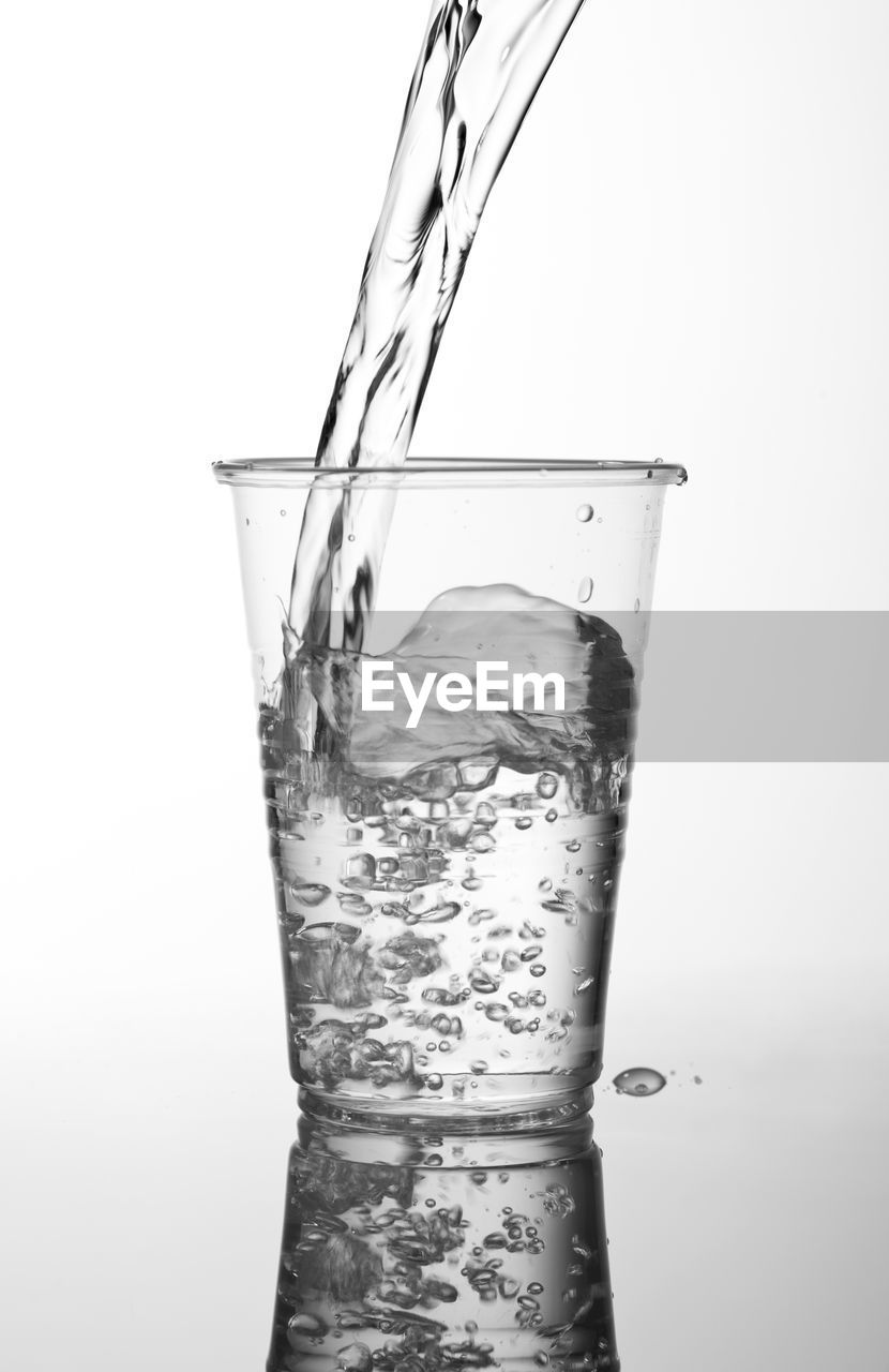 Close-up of water splashing in drinking glass against white background