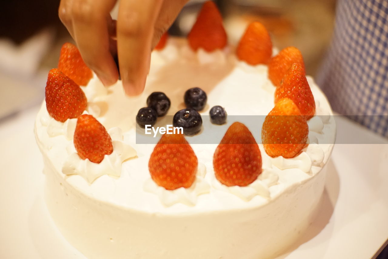 CLOSE-UP OF HAND HOLDING STRAWBERRY CAKE