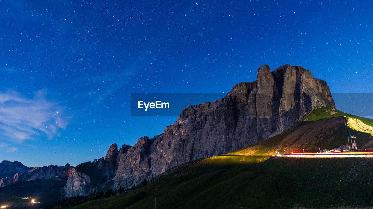 Scenic view of illuminated light trails on road by mountain against sky
