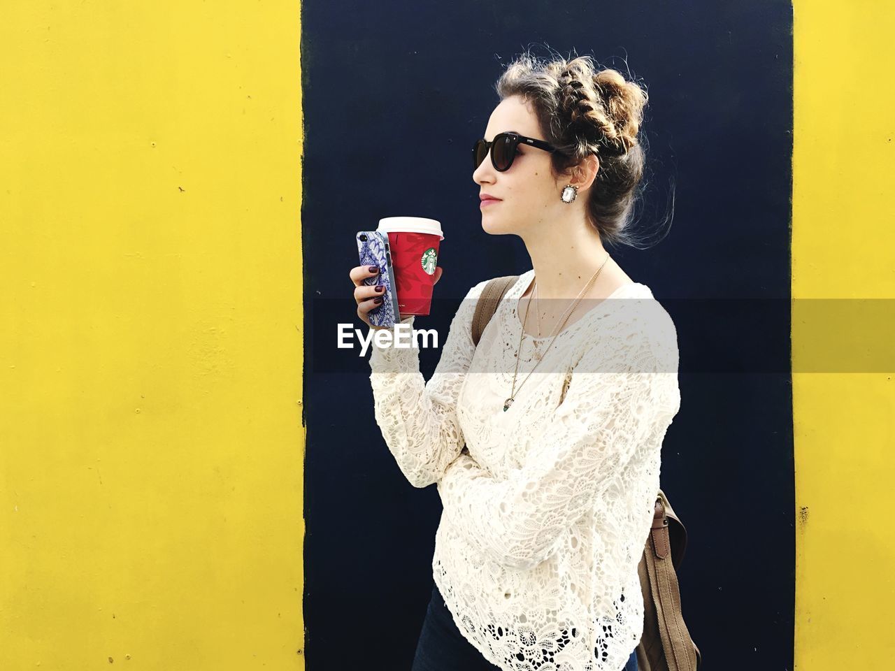 Young woman holding disposable coffee cup against the wall