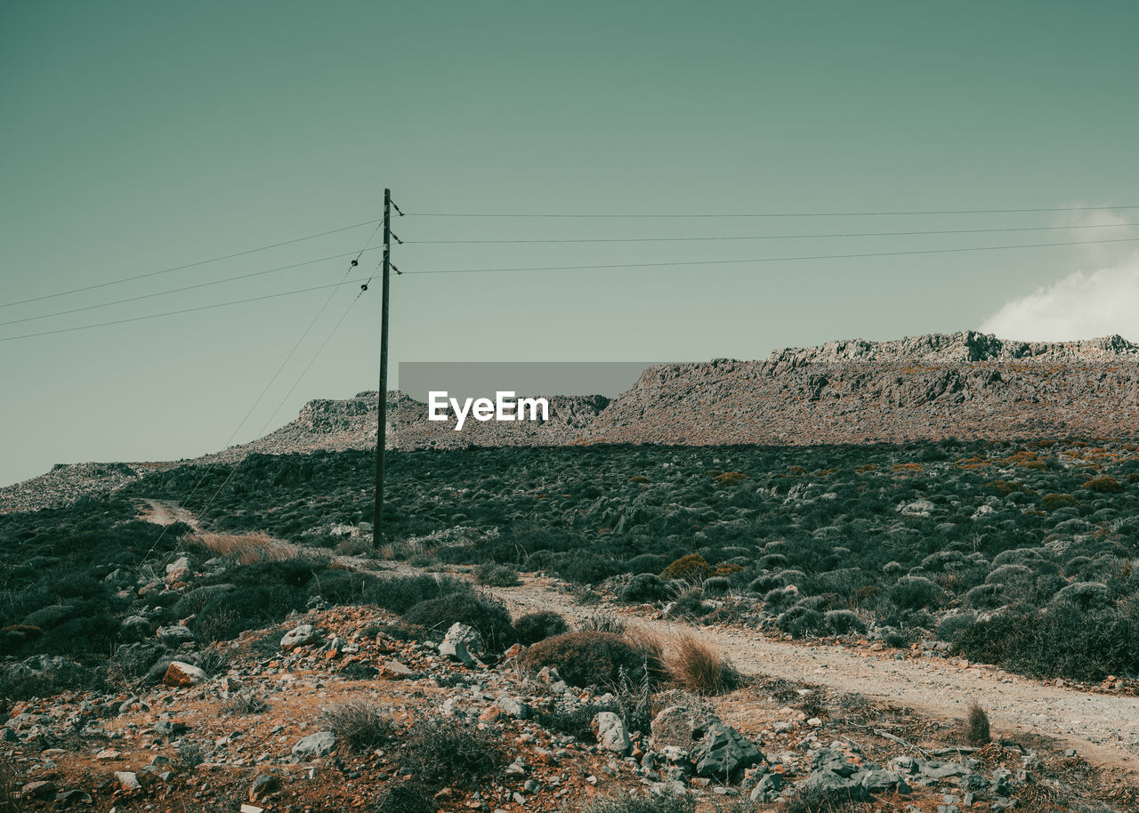 electricity, cable, sky, electricity pylon, technology, power line, nature, environment, landscape, power supply, land, power generation, horizon, no people, scenics - nature, mountain, beauty in nature, rock, non-urban scene, outdoors, day, tranquility, tranquil scene, clear sky, soil, telephone pole, plant, remote, telephone line, communication, sea
