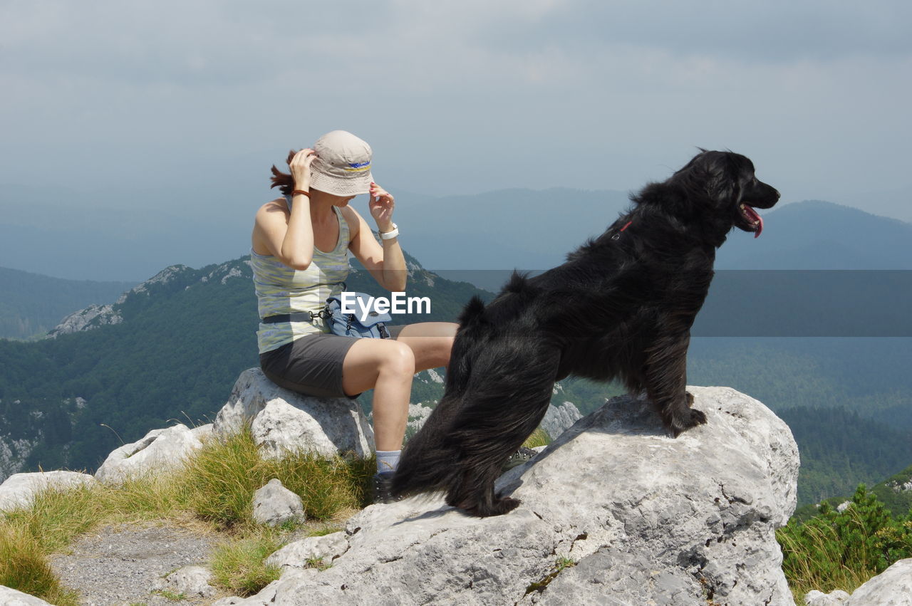 Woman sitting with flat-coated retriever on mountain peak against sky