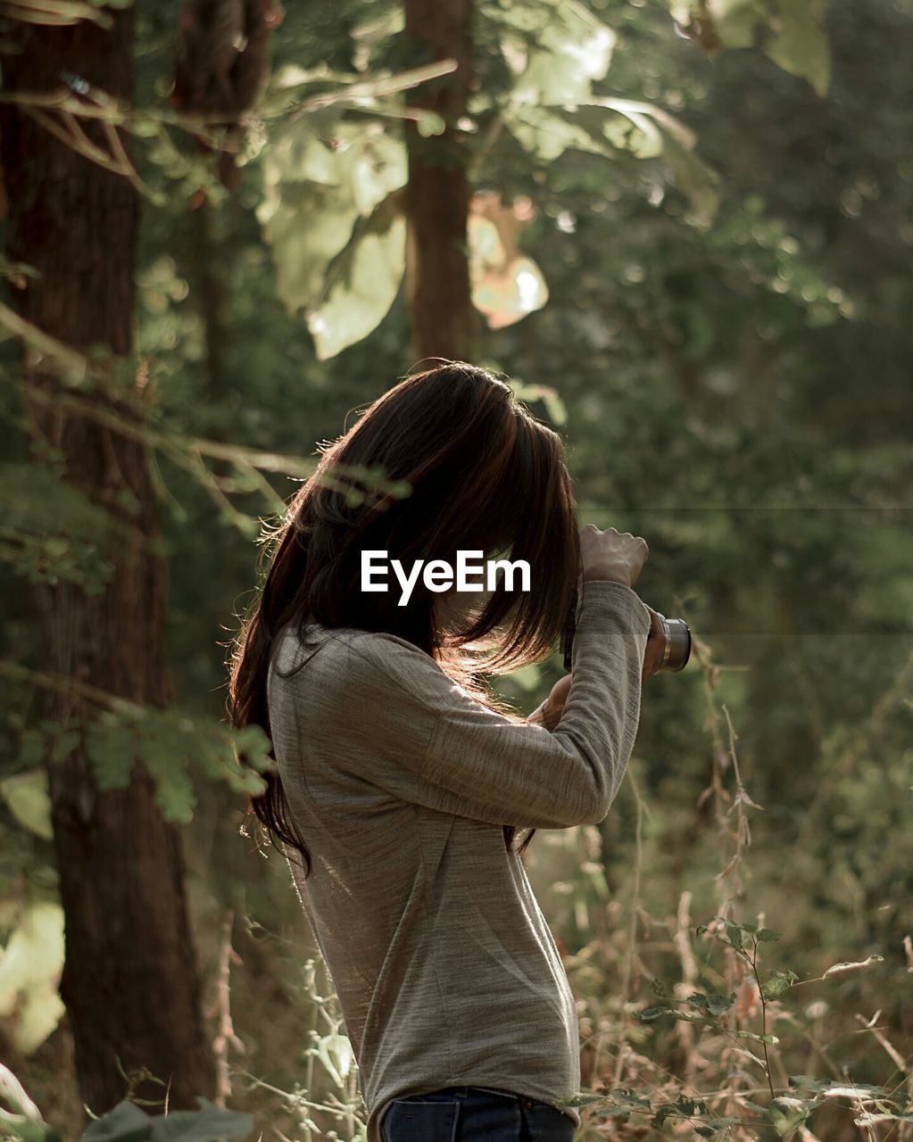 Side view of young woman photographing through camera at forest