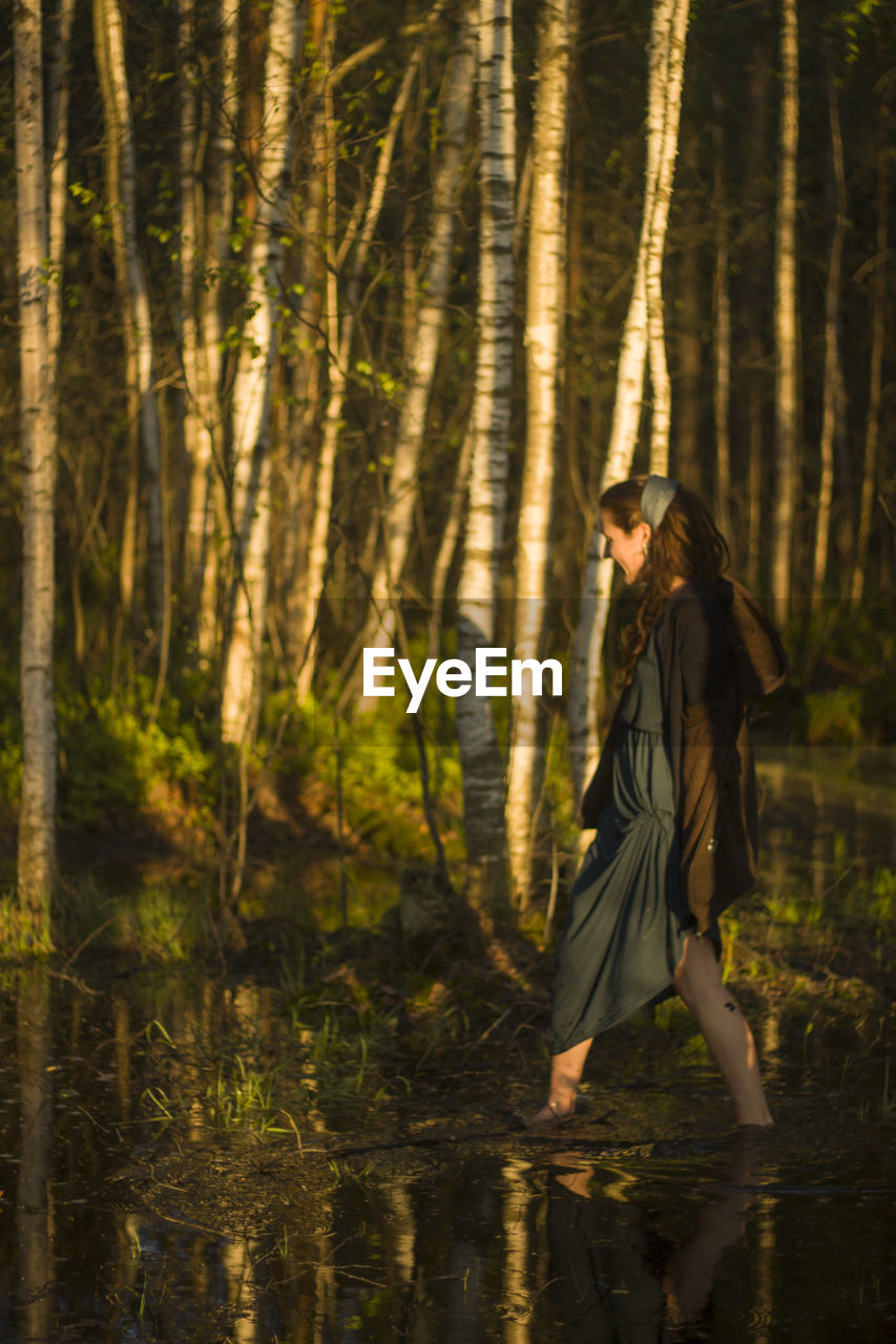 Side view of woman walking in lake against trees at forest