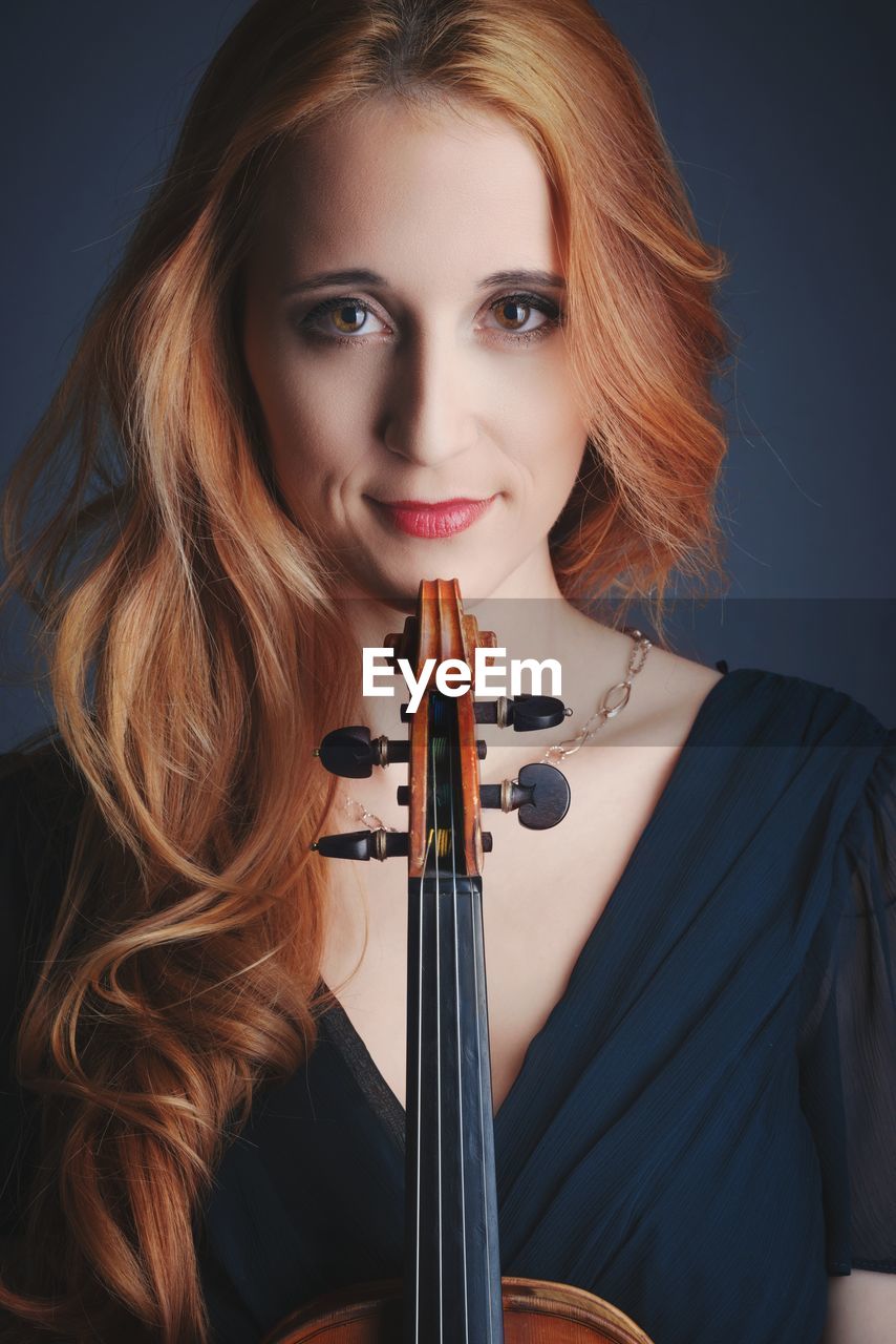 Portrait of young woman with violin against colored background