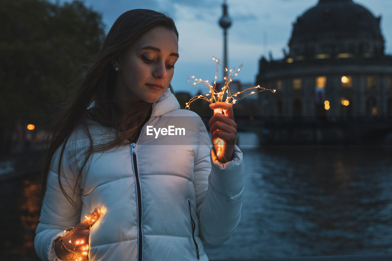 Young woman holding illuminated lights with fernsehturm in background