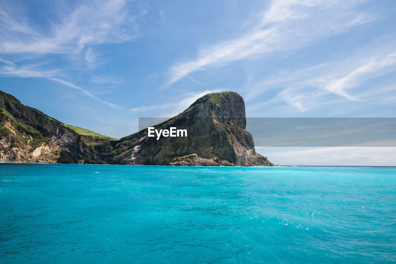 Scenic view of sea by mountain against sky