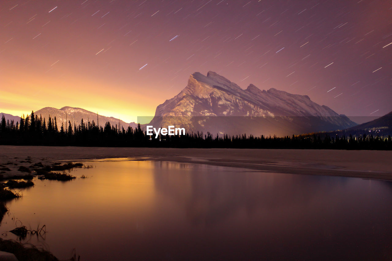 Scenic view of lake and mountains against star trail at night