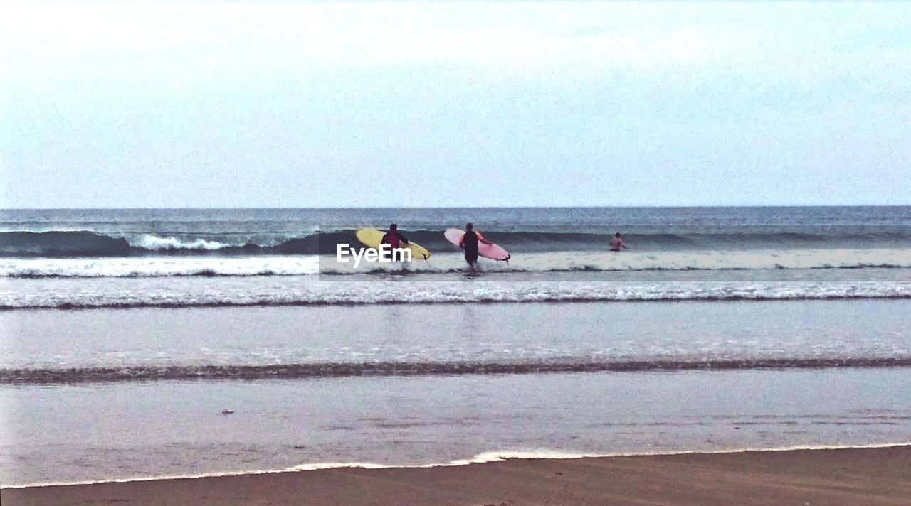 People with surfboards at beach against sky