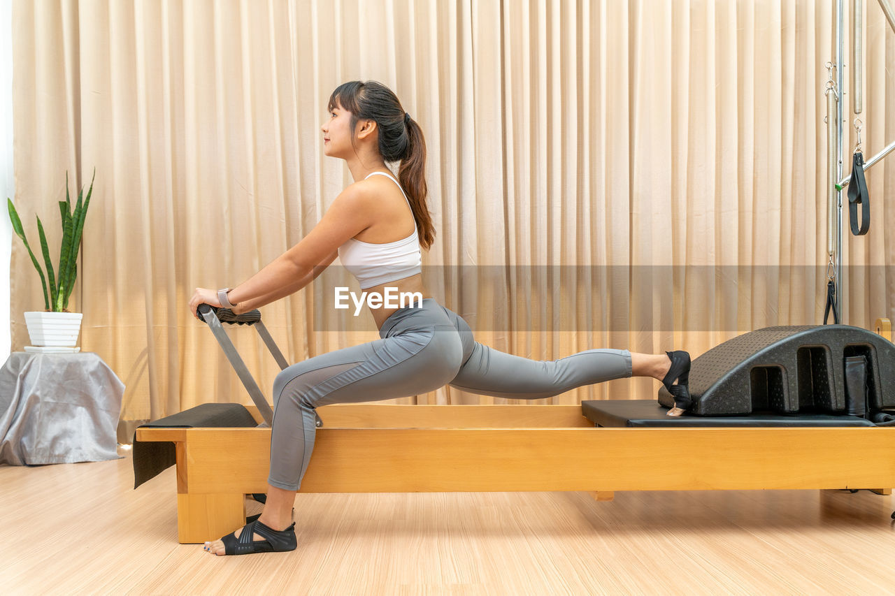 Young asian woman working on pilates reformer machine during her health exercise training