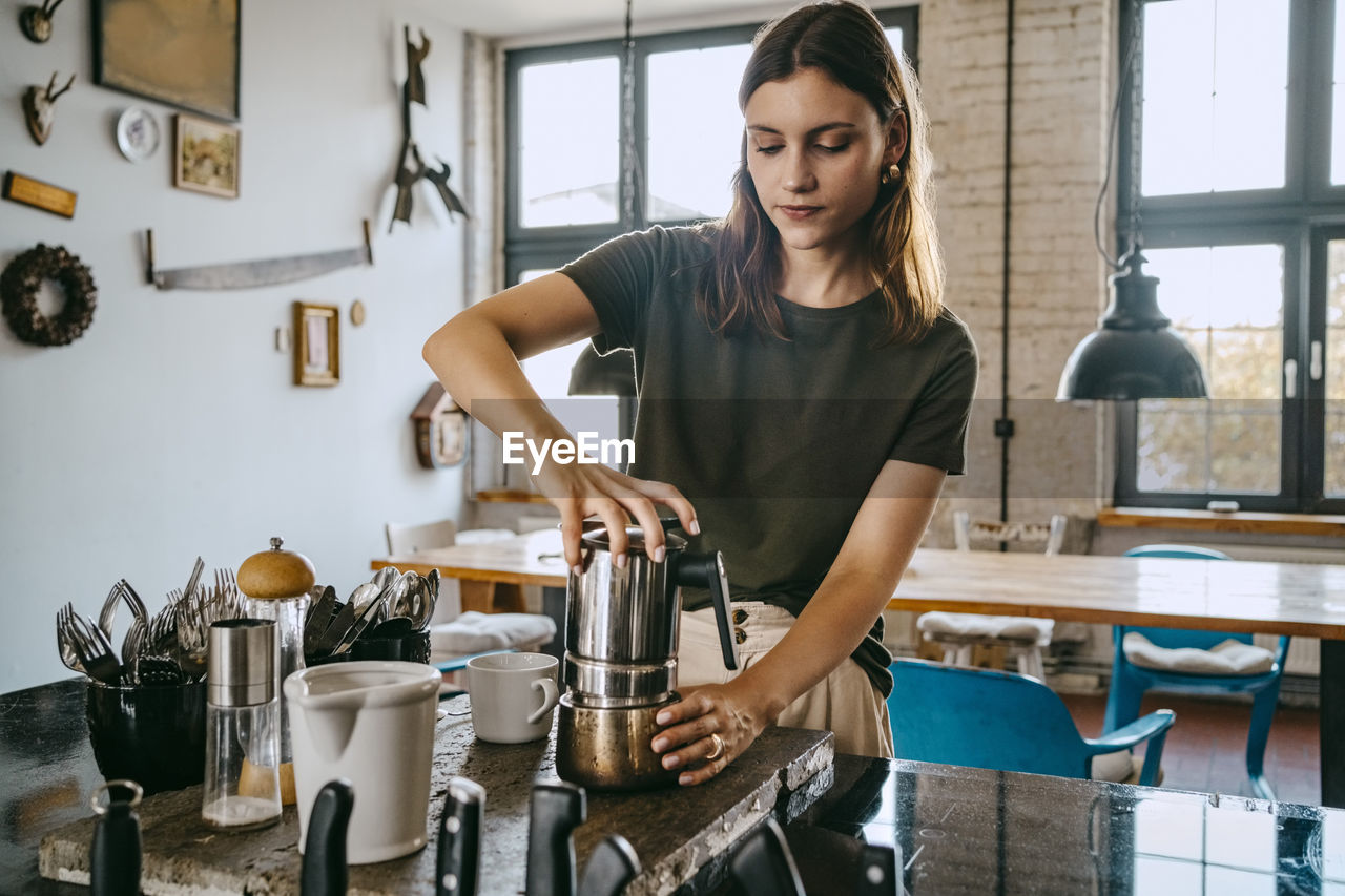 Female entrepreneur tightening kettle while preparing coffee in studio