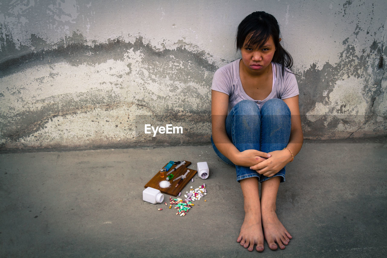 Depressed teenage girl sitting by narcotics against wall