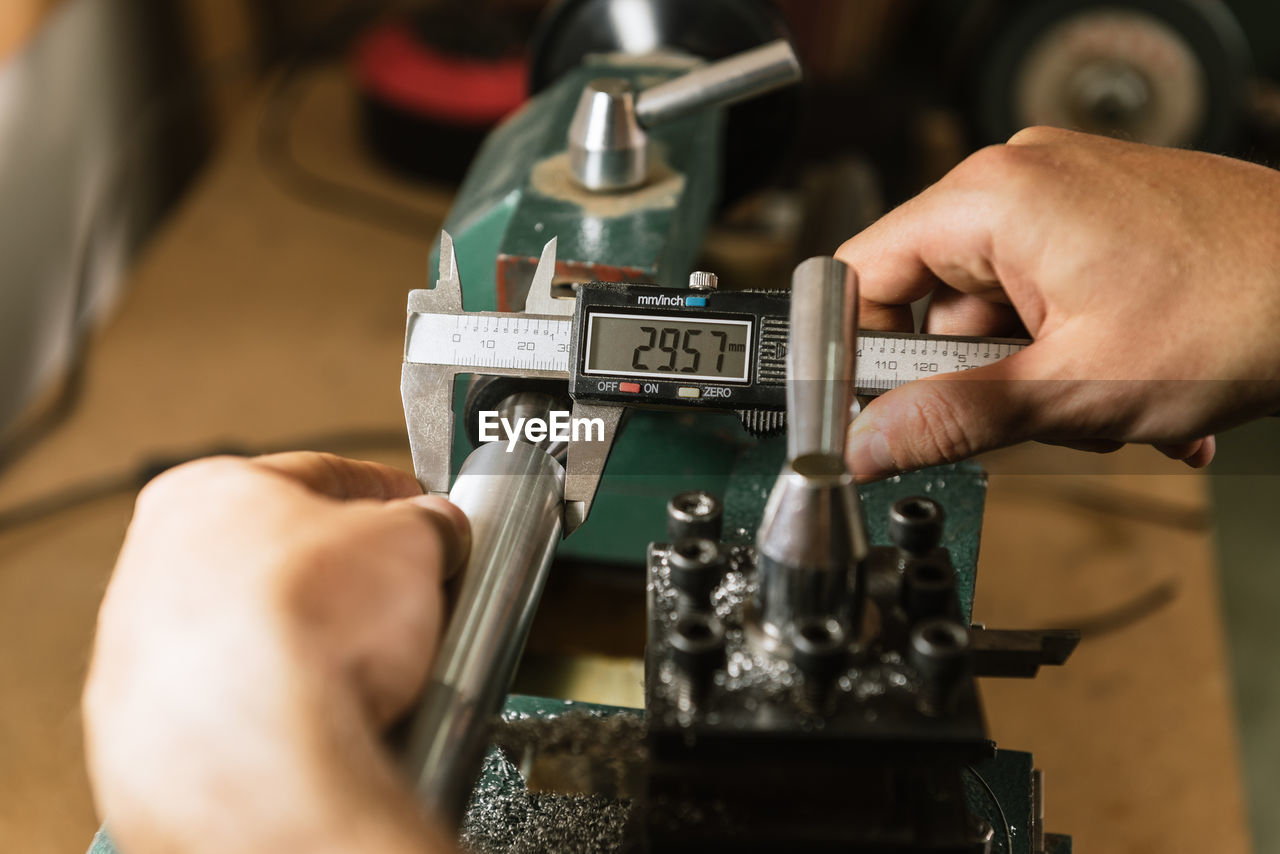 Unrecognizable technician standing at workbench and using caliper for precise gauging while working in shabby workshop