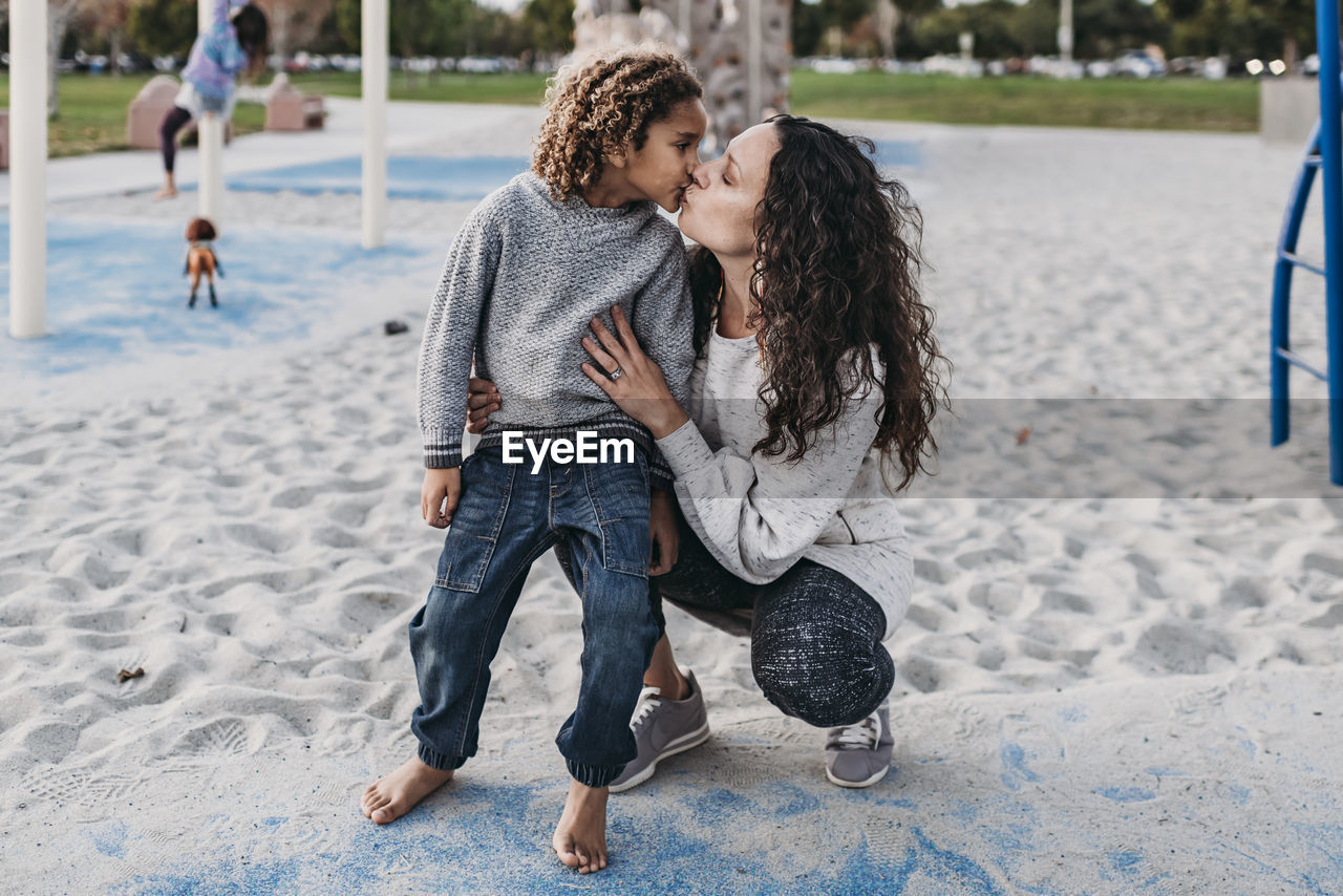 Mother giving son a kiss while playing on playground at dusk