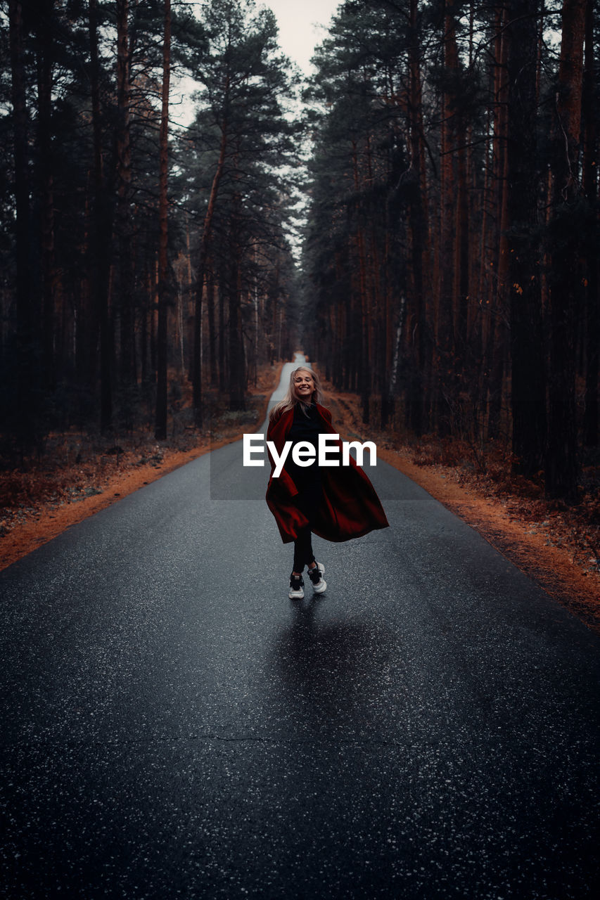 Woman walking on road amidst trees in forest